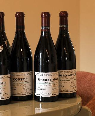 A collection of Domaine de la Romanée-Conti wine bottles with classic cream labels arranged on a smooth table.