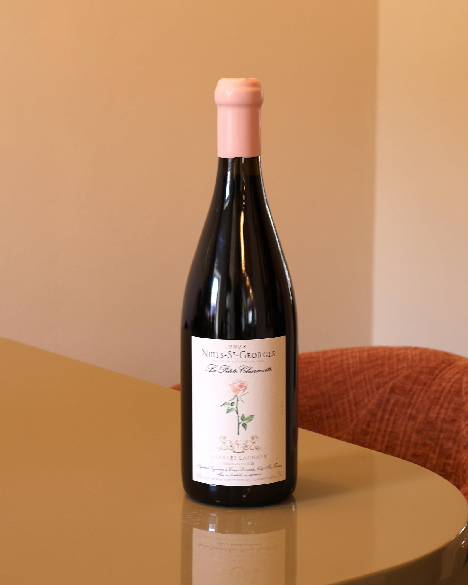 Bottiglia di vino rosso Charles Lachaux Nuits-Saint-Georges 2023 con capsula rosa su tavolo lucido.
