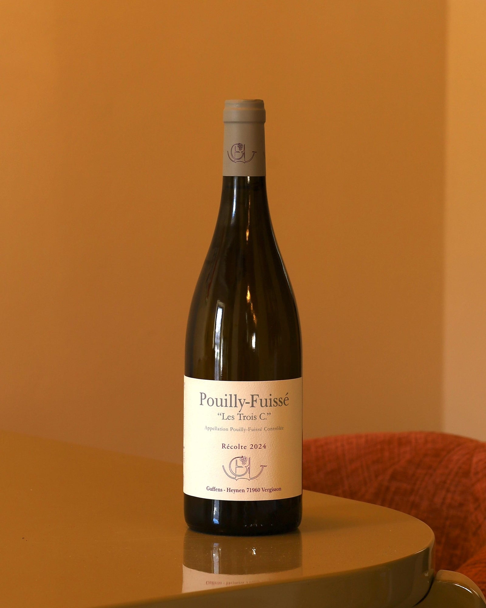 Bottiglia di vino bianco Guffens-Heynen Pouilly-Fuissé Les Trois C. 2024 da 0,75l con etichetta bianca su sfondo color pesca.