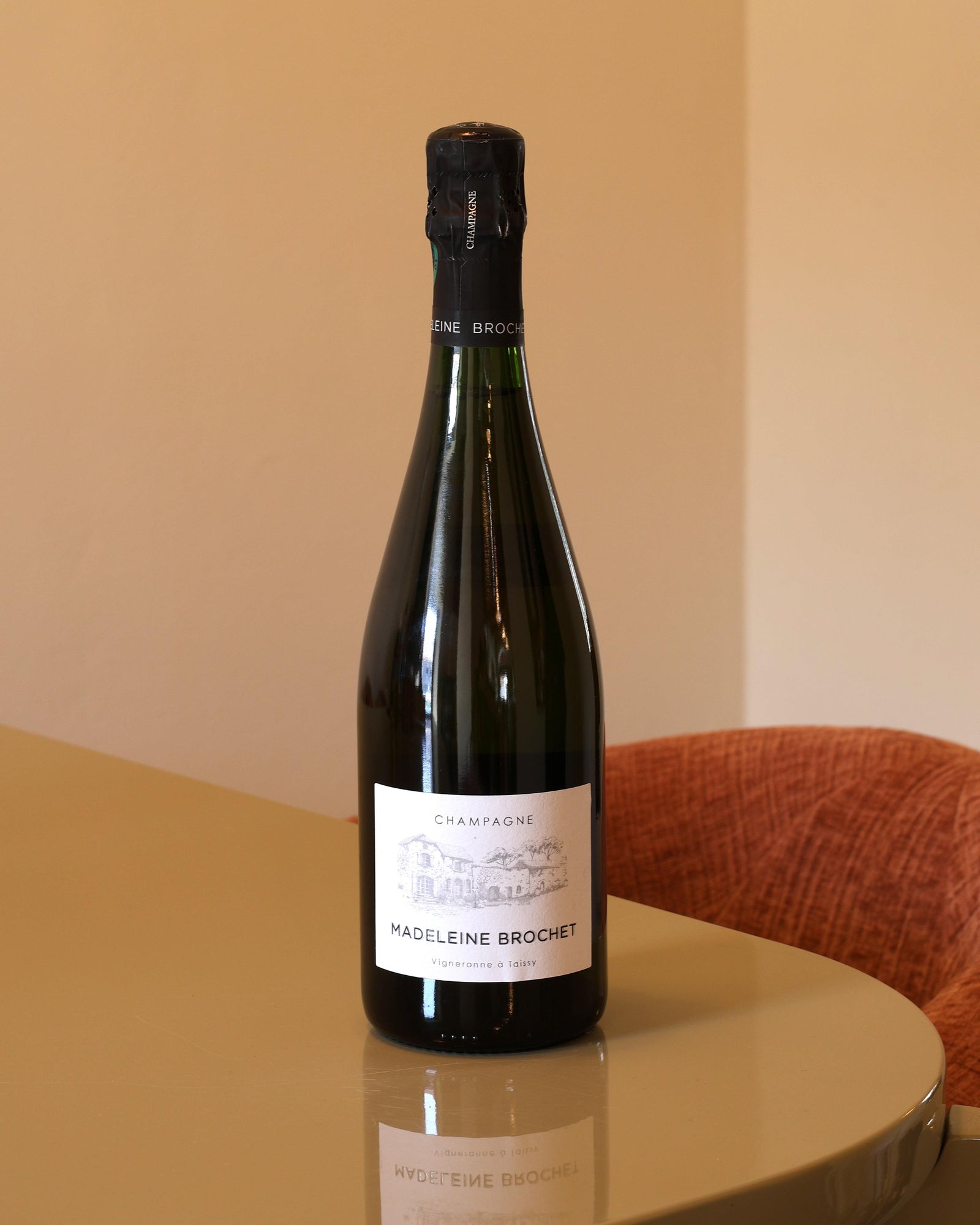 Bottiglia di Champagne Madeleine Brochet Millesime Extra Brut 2020 da 0,75l con etichetta bianca su tavolo lucido.