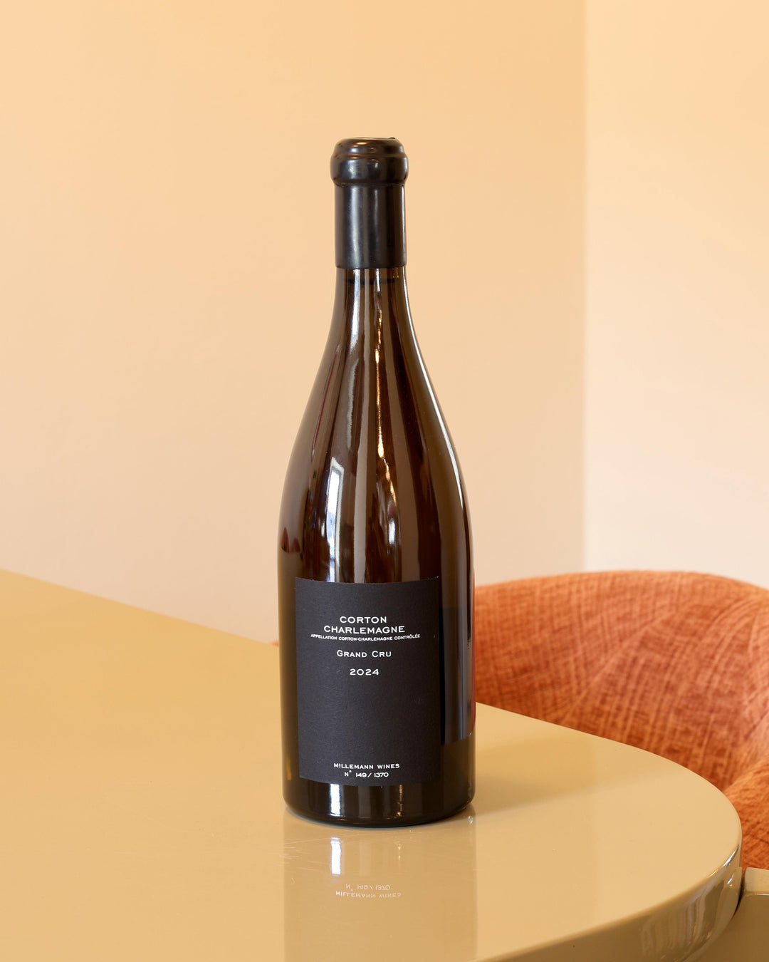 Bottiglia di vino bianco Millemann Corton-Charlemagne Grand Cru 2024 con etichetta nera minimalista su tavolo lucido.