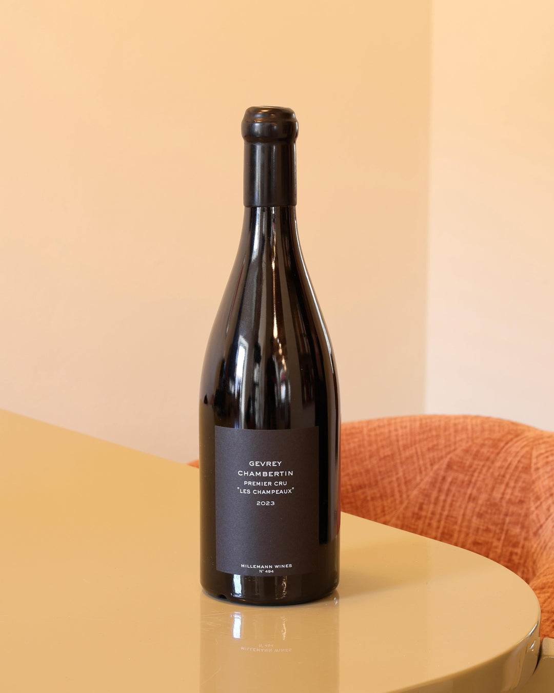 Bottiglia di vino rosso Millemann Gevrey-Chambertin Premier Cru 2023 con etichetta nera minimalista su tavolo lucido.