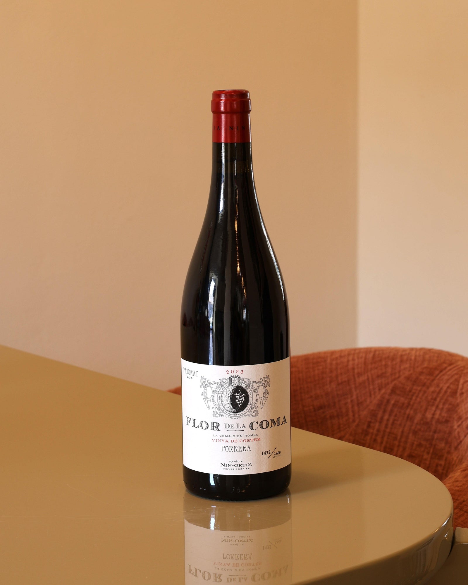 Bottiglia di vino rosso Nin Ortiz Flor de la Coma 2023 da 0,75l con etichetta chiara su tavolo riflettente.