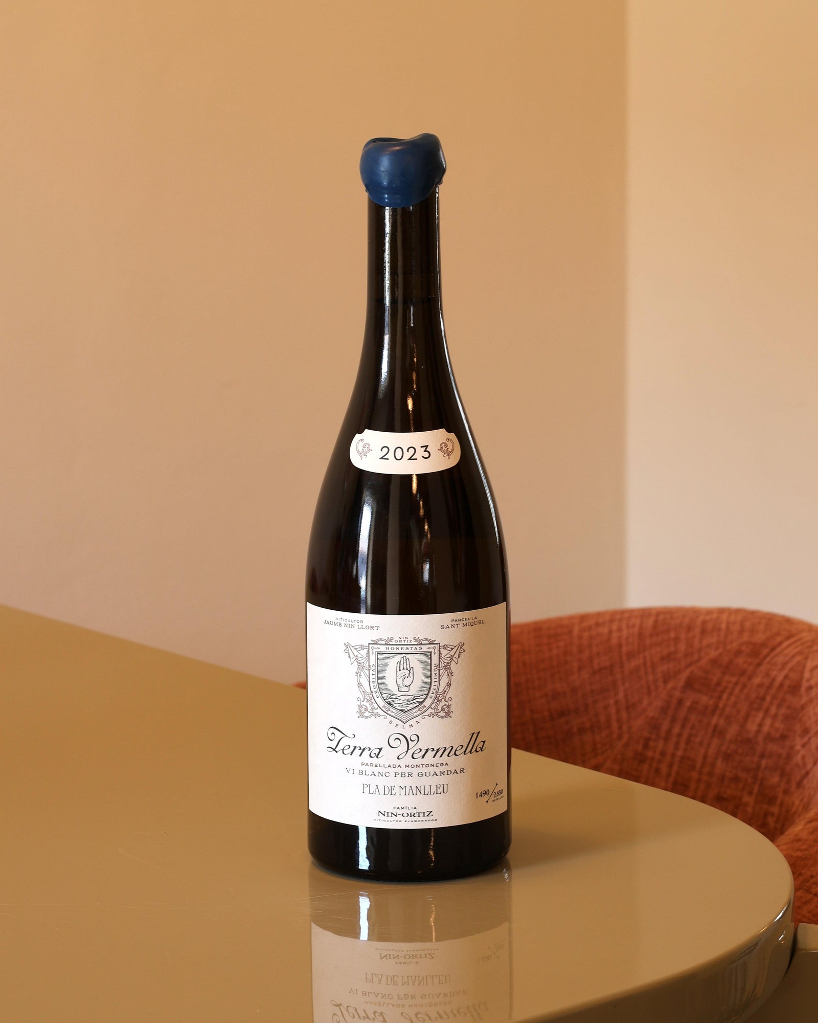 Bottiglia di vino bianco Nin Ortiz Terra Vermella 2023 da 0,75l con tappo in ceralacca blu su tavolo lucido.