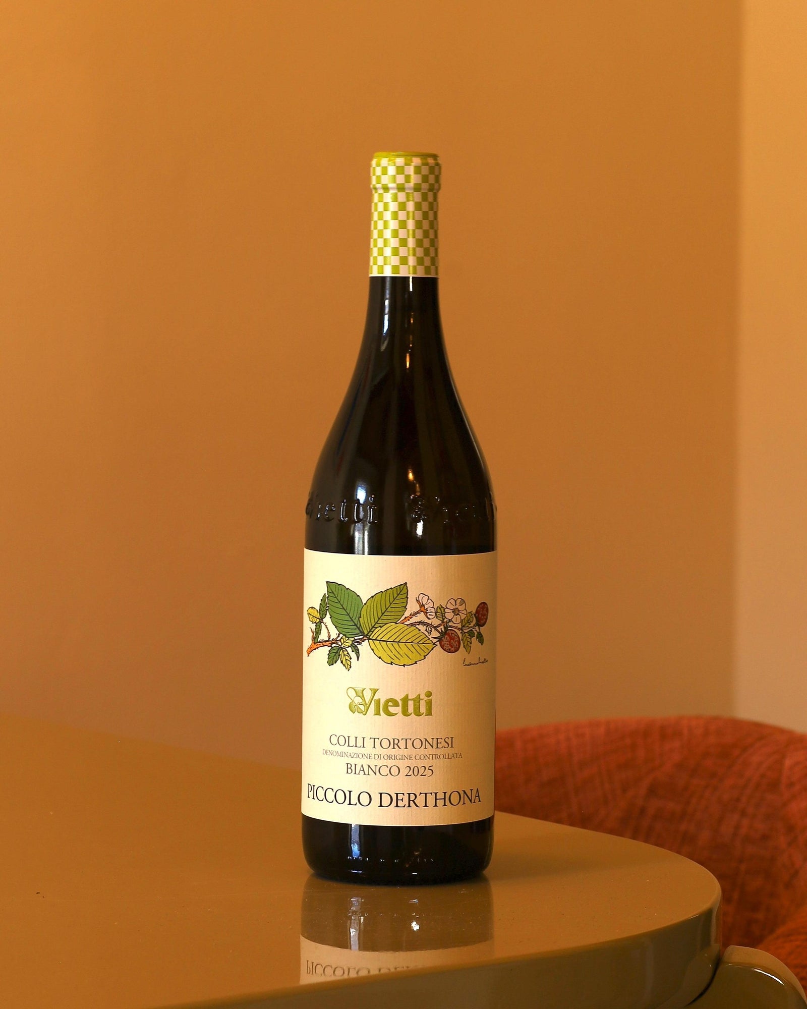 Bottiglia di vino bianco Vietti Piccolo Derthona 2025 con etichetta illustrata e capsula verde a scacchi su tavolo lucido.