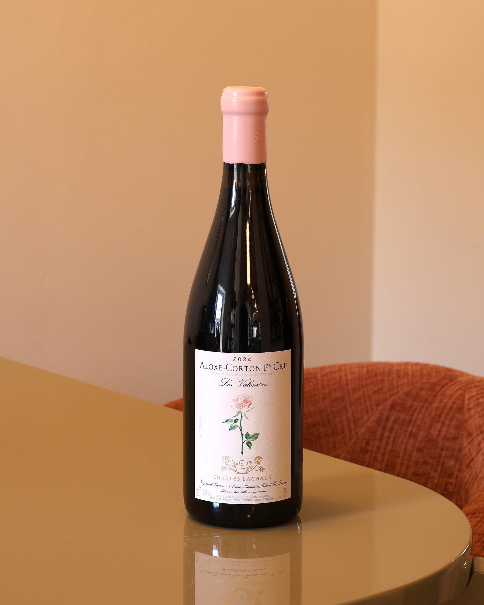 Bottiglia di vino rosso Charles Lachaux Aloxe-Corton 1er Cru 2024 con capsula rosa su tavolo lucido.